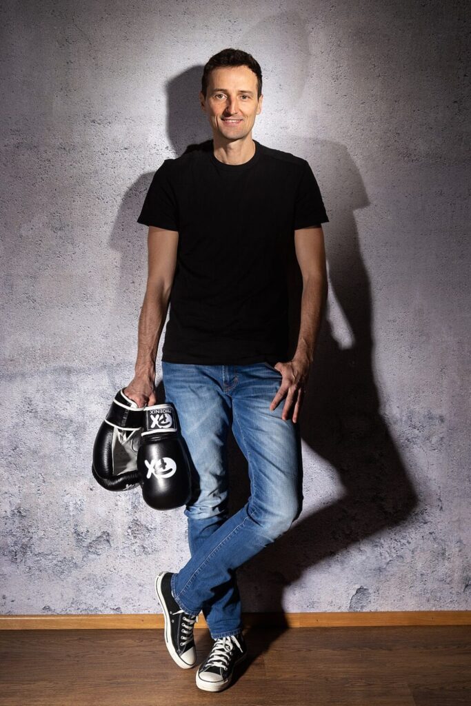 Roland Conar, 13-facher Kickbox-Weltmeister, mit Boxhandschuhen vor grauer Wand