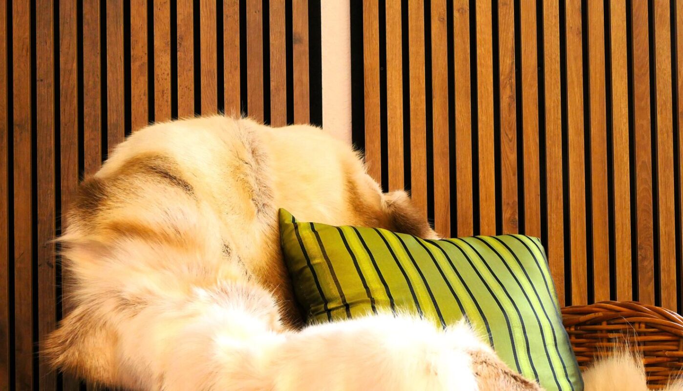 Holzverkleidete Wand mit dekorativem Lammfell und grünem Zierkissen in der Ausstellung von Holz Hertel